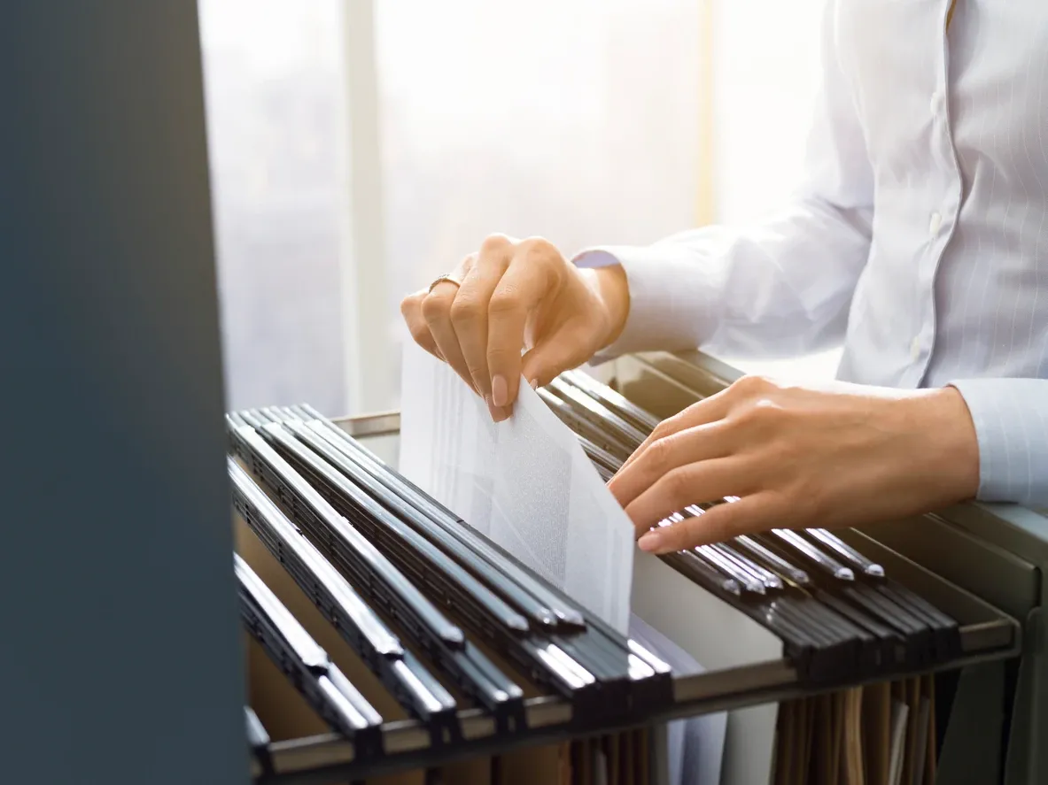 Professional female office clerk searching files and paperwork in the filing cabinet.