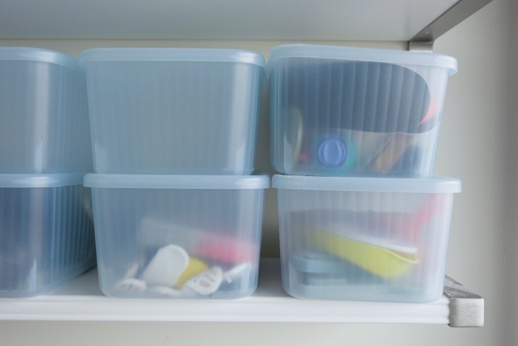 A series of stacked, translucent plastic storage containers on a shelf with items inside them.