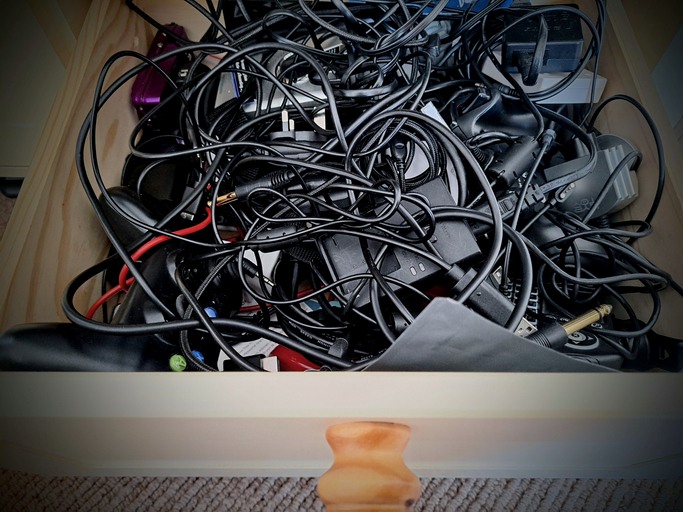 A jumbled mess of cables sits in a wooden drawer.