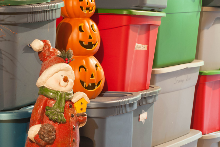 Gray, red, and green plastic storage bins are stacked in rows, with a decorative snowman and a stack of pumpkins beside.